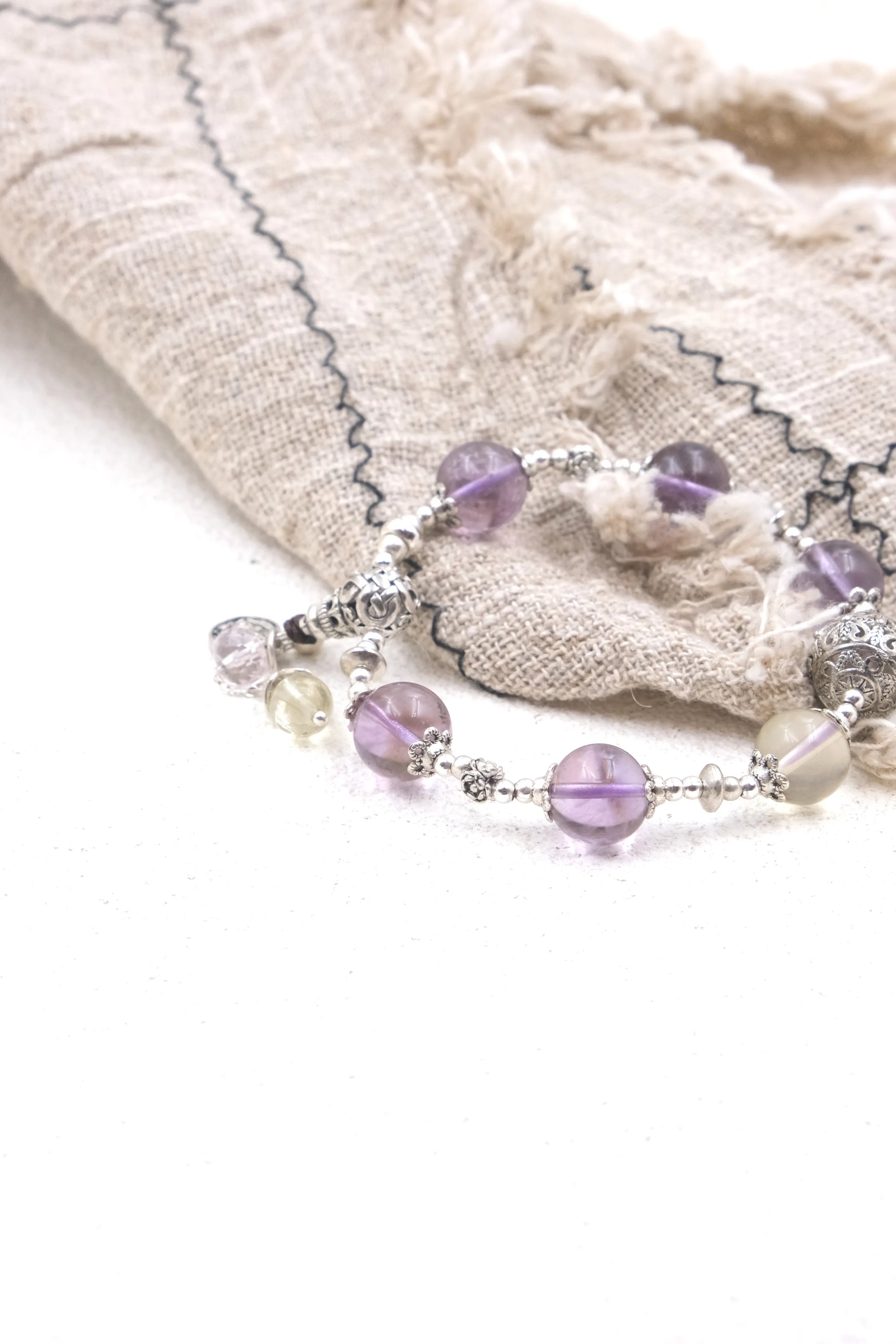 Vajra Bell Crystal Energy Bracelet with purple and white beads on a textured fabric background