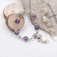 Vajra Bell Crystal Energy Bracelet Beaded bracelet with purple and clear beads on a white surface with fabric and wood slice in the background