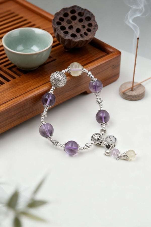 Bracelet with purple beads and silver accents on a wooden tray with tea cup and incense.