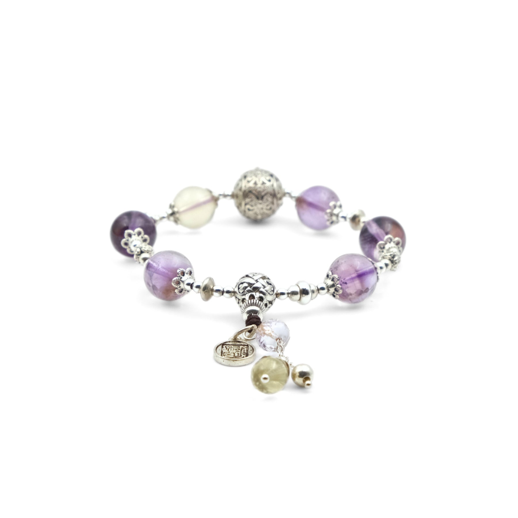 A Vajra Bell Crystal Energy Bracelet featuring amethyst beads that display a beautiful range of purple hues. These amethyst beads are interspersed with other beads, including a light - colored one and an intricately designed silver bead. Silver - toned floral - like accents accompany the beads.