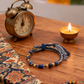 Vintage alarm clock, Lapis Lazuli Woven Bracelet, and stones on a wooden surface with a colorful fabric background.