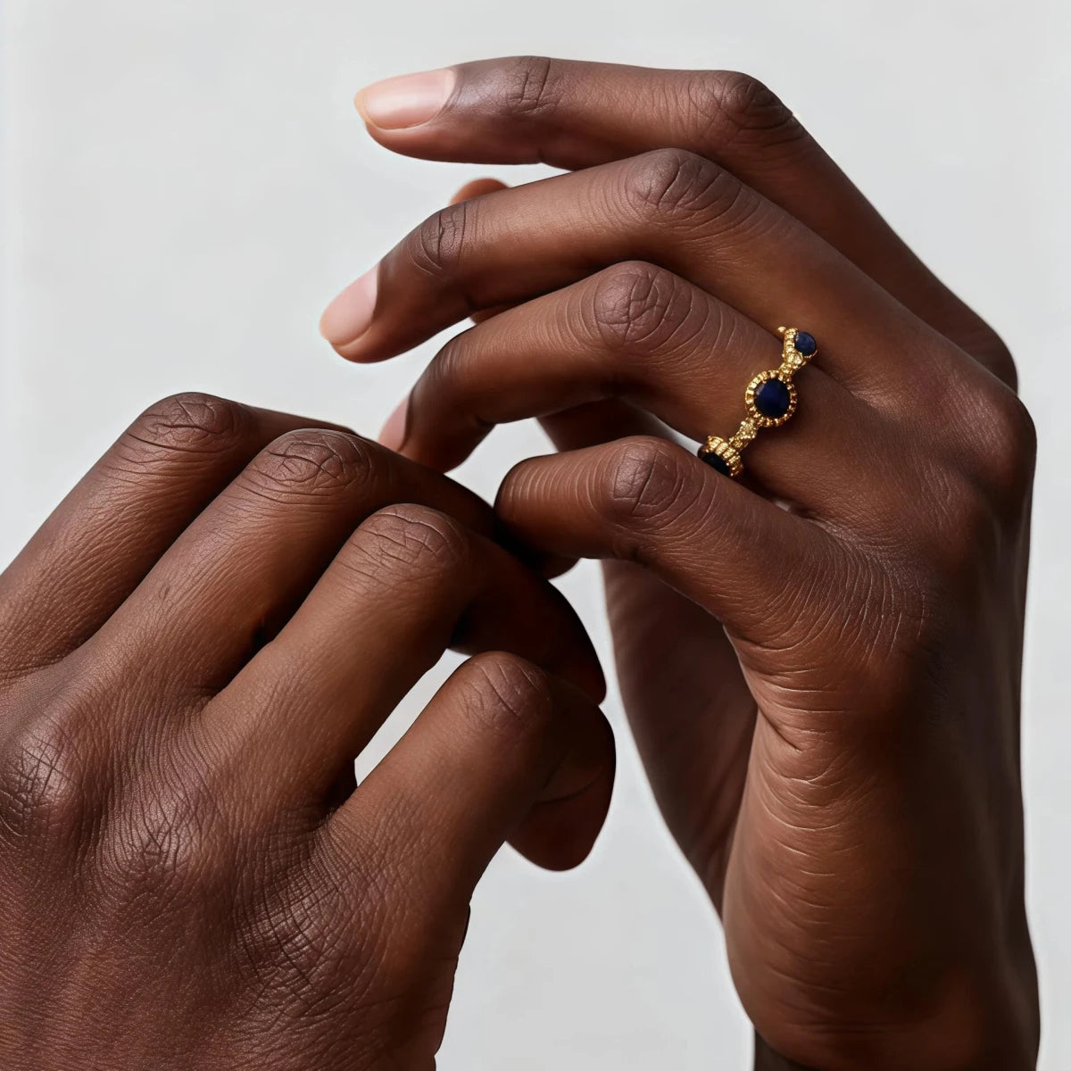 Close-up of a hand wearing a gold ring with a blue  Lapis Lazuli gemstone on a neutral background