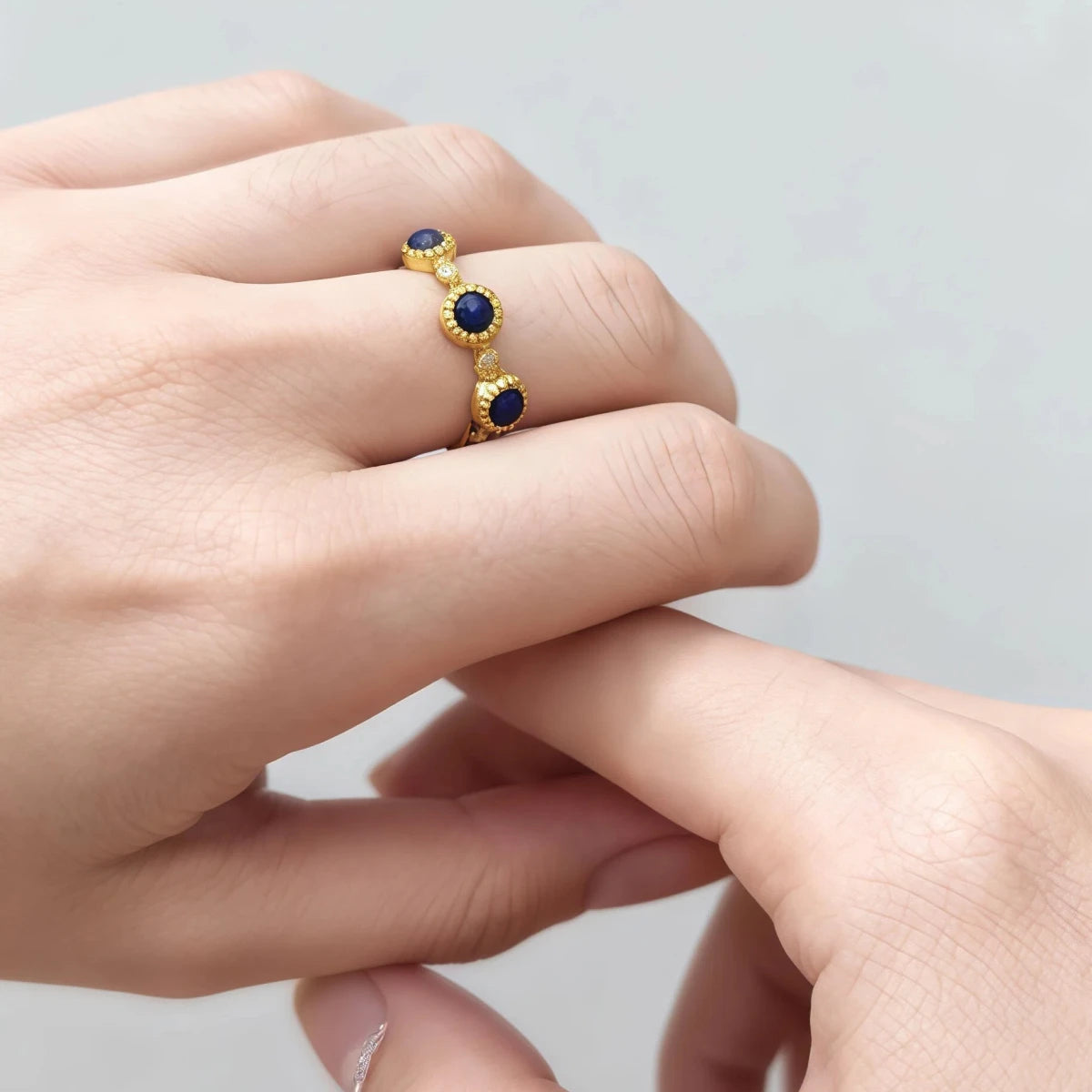 Gold ring with blue Lapis Lazuli stones on a finger against a neutral background