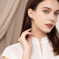 A woman wearing elegant golden hoop earrings with blue lapis lazuli accents, dressed in a white top, against a soft neutral-toned curtain background.