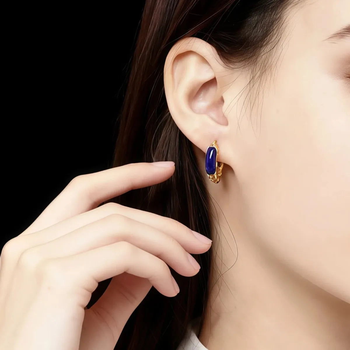 Close-up of a person wearing a gold earring with a blue Lapis_Lazuli_Vintage gemstone on a black background